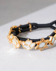 A black braided cord bracelet featuring gold-toned metal charms including crescent moons and six-pointed stars, displayed on a light gray surface.