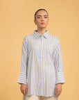 A full-length shot of a woman wearing a blue and white striped long button-down shirt.