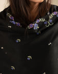 Close-up of pastel embroidery on black shawl fabric showing stitch detail and texture.