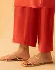 Close-up of the red straight-fit trousers, highlighting the soft fabric texture and ankle-length cut.