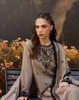 A woman wearing a grey and black embroidered traditional outfit sits on a bench in front of a dark forest backdrop with flowers.