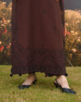 A person outdoors on grass wearing a long dark brown skirt with black lace trim and pom-pom detailing, paired with black slingback heels.
