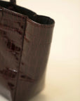 Dark chocolate patent tote bag featuring textured croc pattern and structured silhouette with sturdy handles.