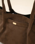 Front view of a brown fabric handbag featuring double handles and a minimal clasp detail