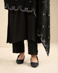 Lower hem view of the shawl with embroidered edge, paired with black trousers and heels.