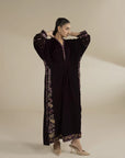 Model wearing dark velvet embroidered kaftan with gold detailing, full-length front view in studio setting