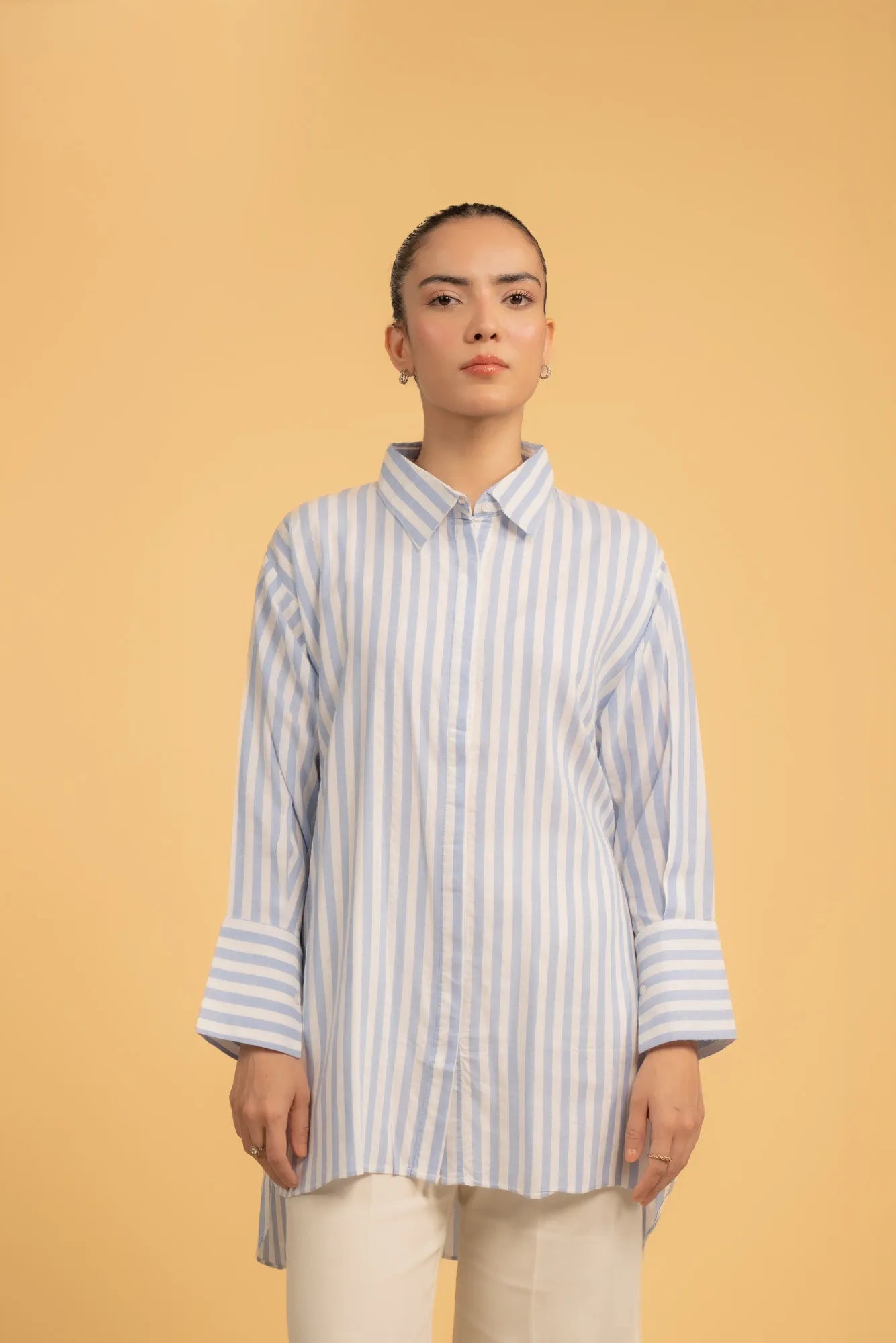 A full-length shot of a woman wearing a blue and white striped long button-down shirt.