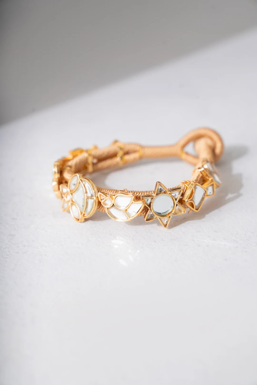 A gold-toned bracelet for women in pakistan with cord band featuring celestial charms including crescent moons and stars with white or pearl-like insets.
