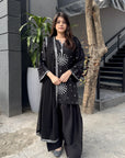 Black embroidered raw silk 3-piece suit styled with farshi shalwar and chiffon dupatta, shown in an outdoor full-look shot.