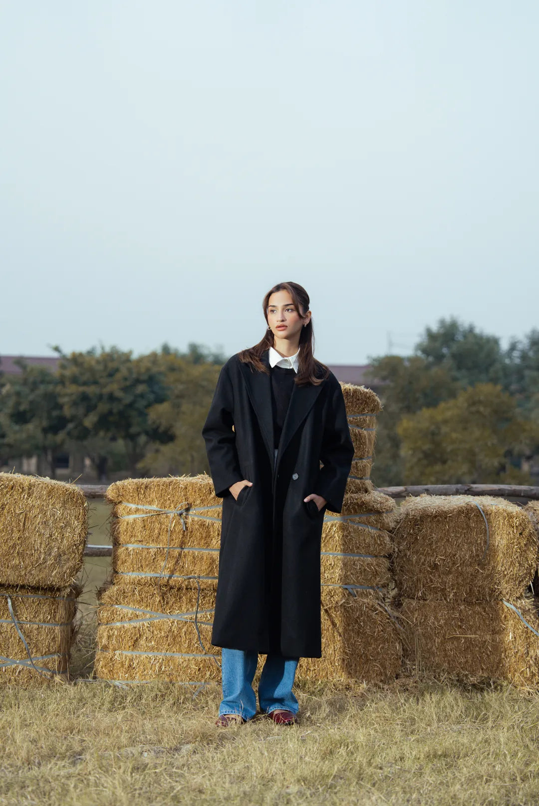 Black longline overcoat for women styled with winter outfit, standing pose