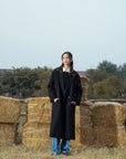 Black longline overcoat for women styled with winter outfit, standing pose