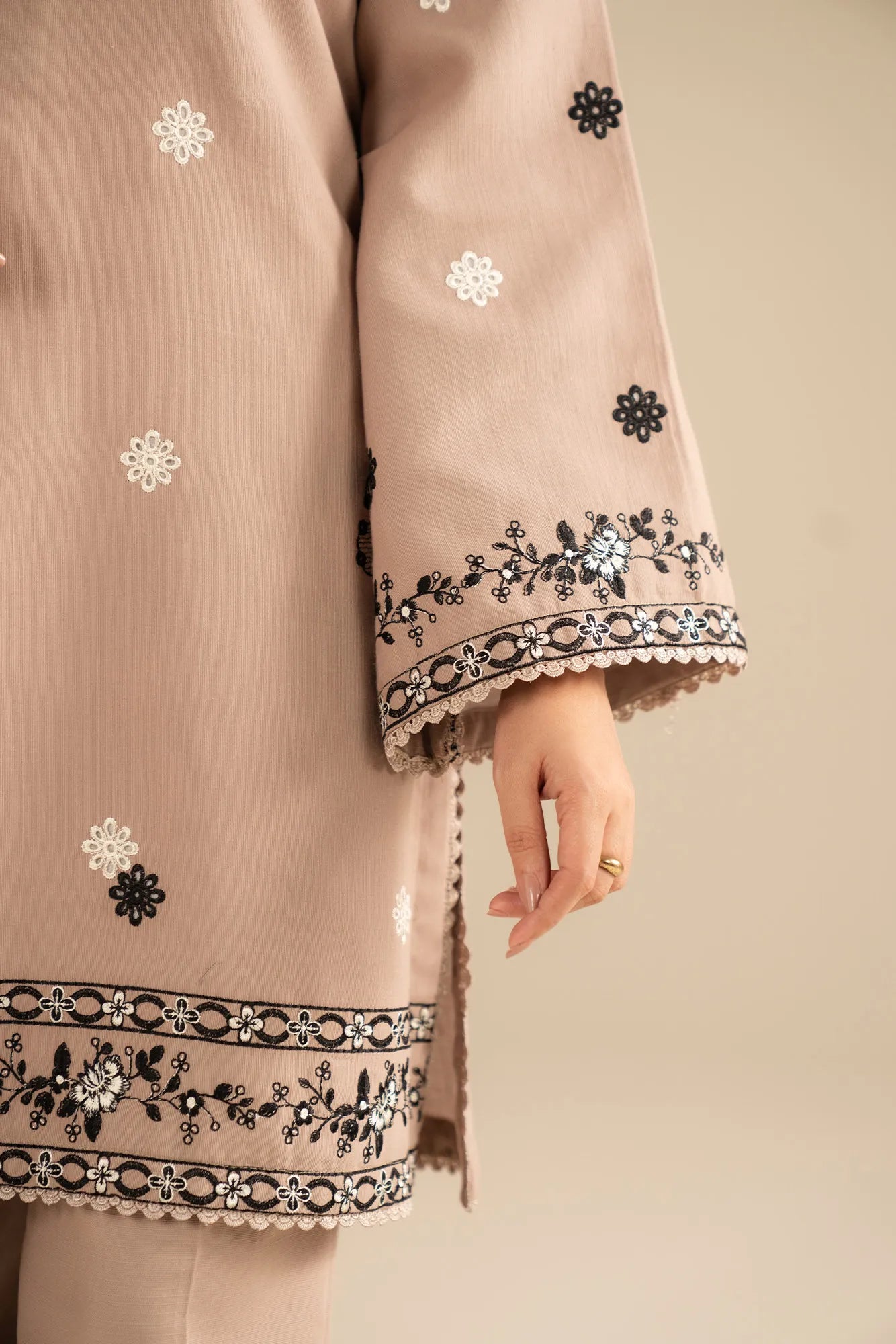 Close-up of black embroidery detailing on beige khaddar shirt front