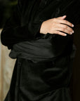 Close-up of black velvet fabric texture and sleeve detail with arms crossed.