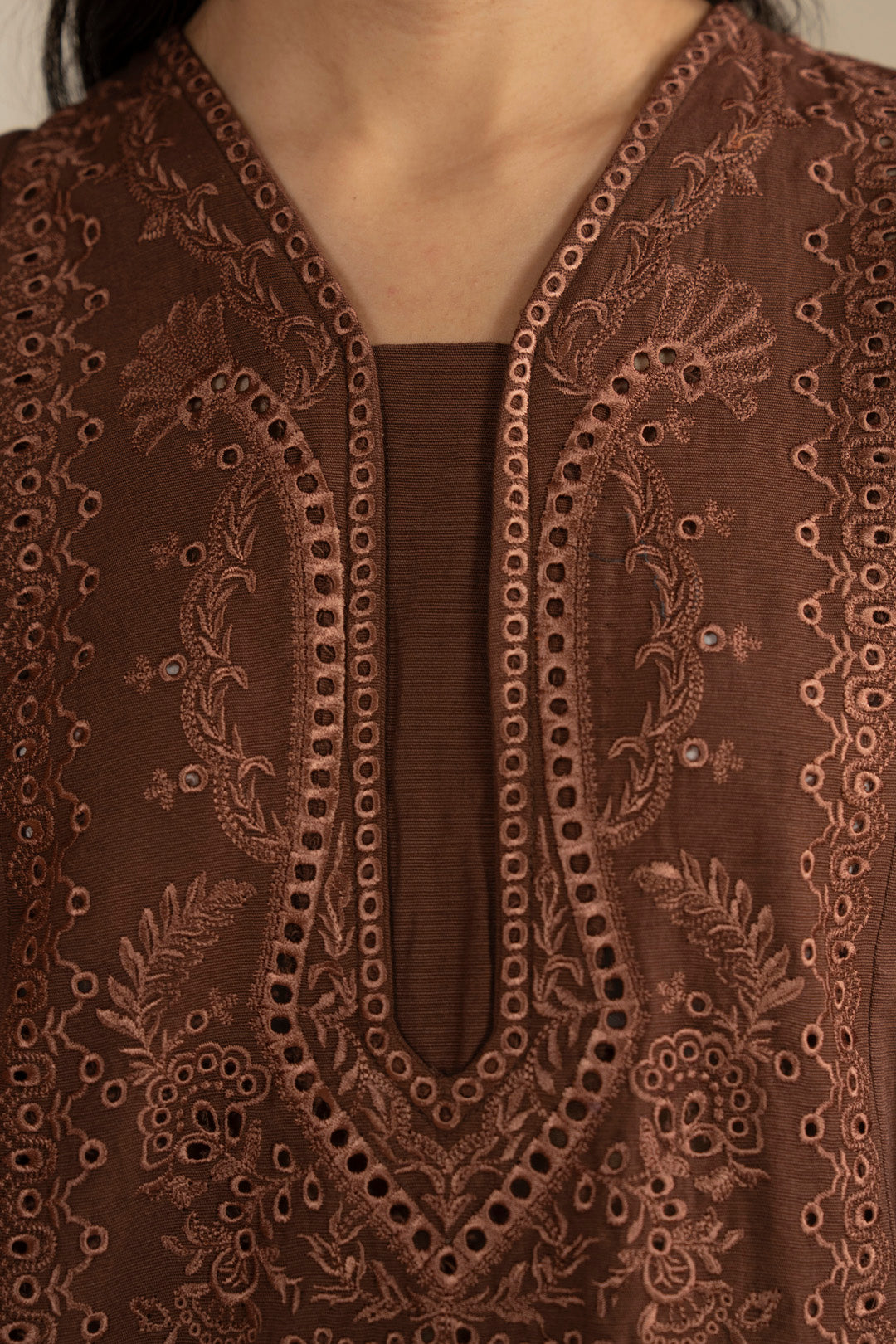 Close-up of embroidered neckline on brown kurta showing intricate front pattern.