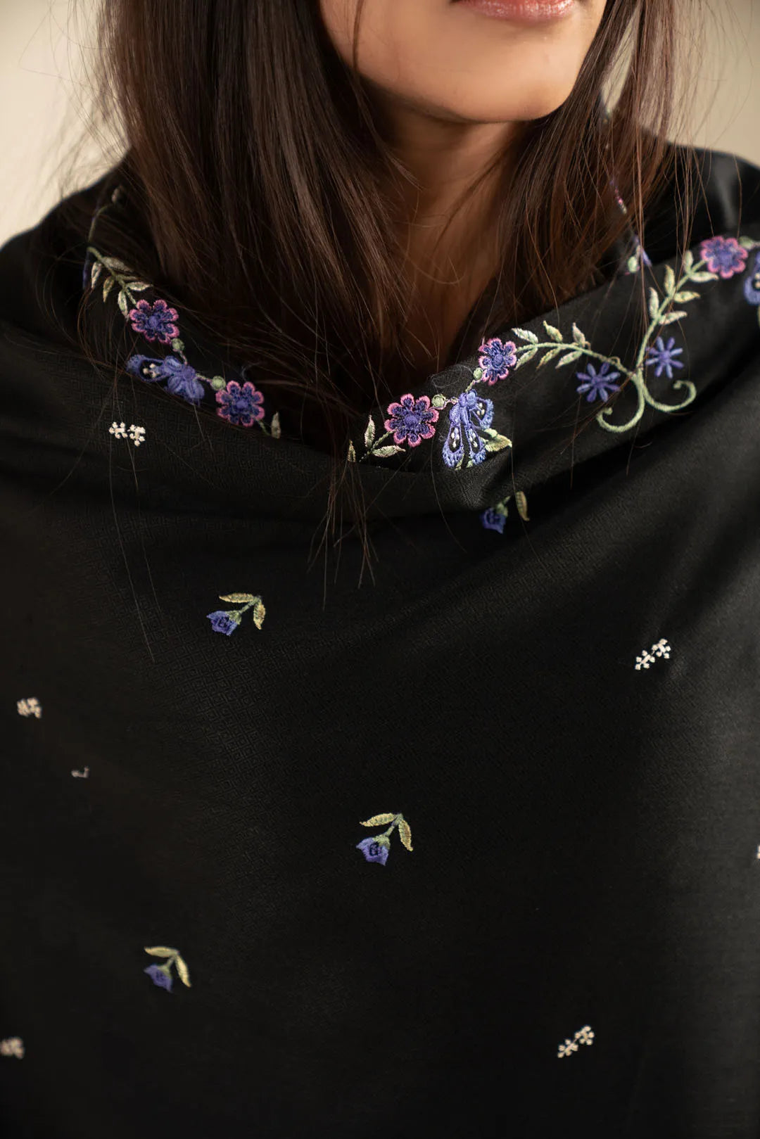 Close-up of pastel embroidery on black shawl fabric showing stitch detail and texture.