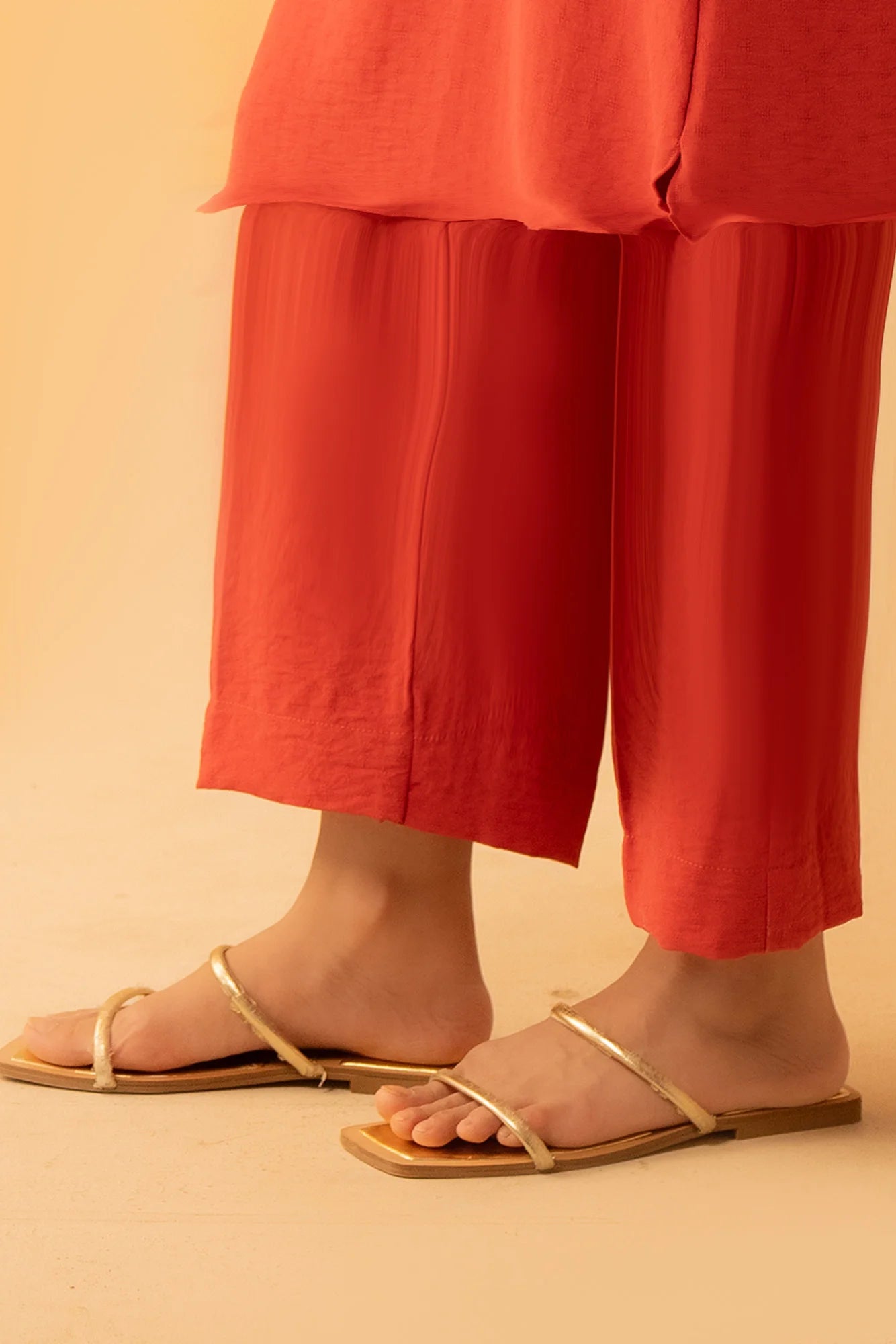 Close-up of the red straight-fit trousers, highlighting the soft fabric texture and ankle-length cut.