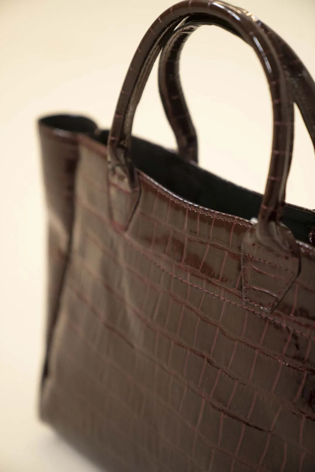 Croc-textured tote bag in shiny brown finish, spacious carryall design photographed from a side-front angle.