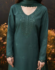 A woman wearing a dark teal green long kurta with intricate matching embroidery and a matching lace-trimmed dupatta, shown against a blurred outdoor background.