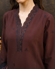 A close-up of a woman wearing a dark brown long-sleeve kurta with a scalloped V-neckline and dark navy blue embroidered floral motifs.