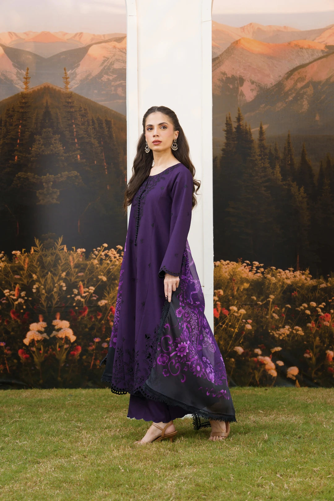 A woman models a deep purple long kurta with matching pants. The kurta features a solid purple upper portion and a sheer black lower skirt panel decorated with purple floral embroidery.