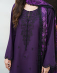 A woman wearing a purple traditional outfit with black embroidered details, a black tassel tie, and a matching purple patterned dupatta.