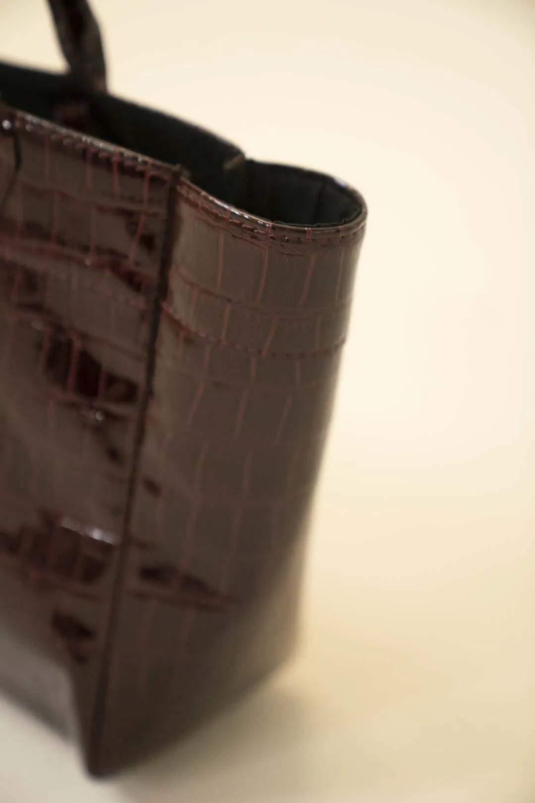 Dark chocolate patent tote bag featuring textured croc pattern and structured silhouette with sturdy handles.