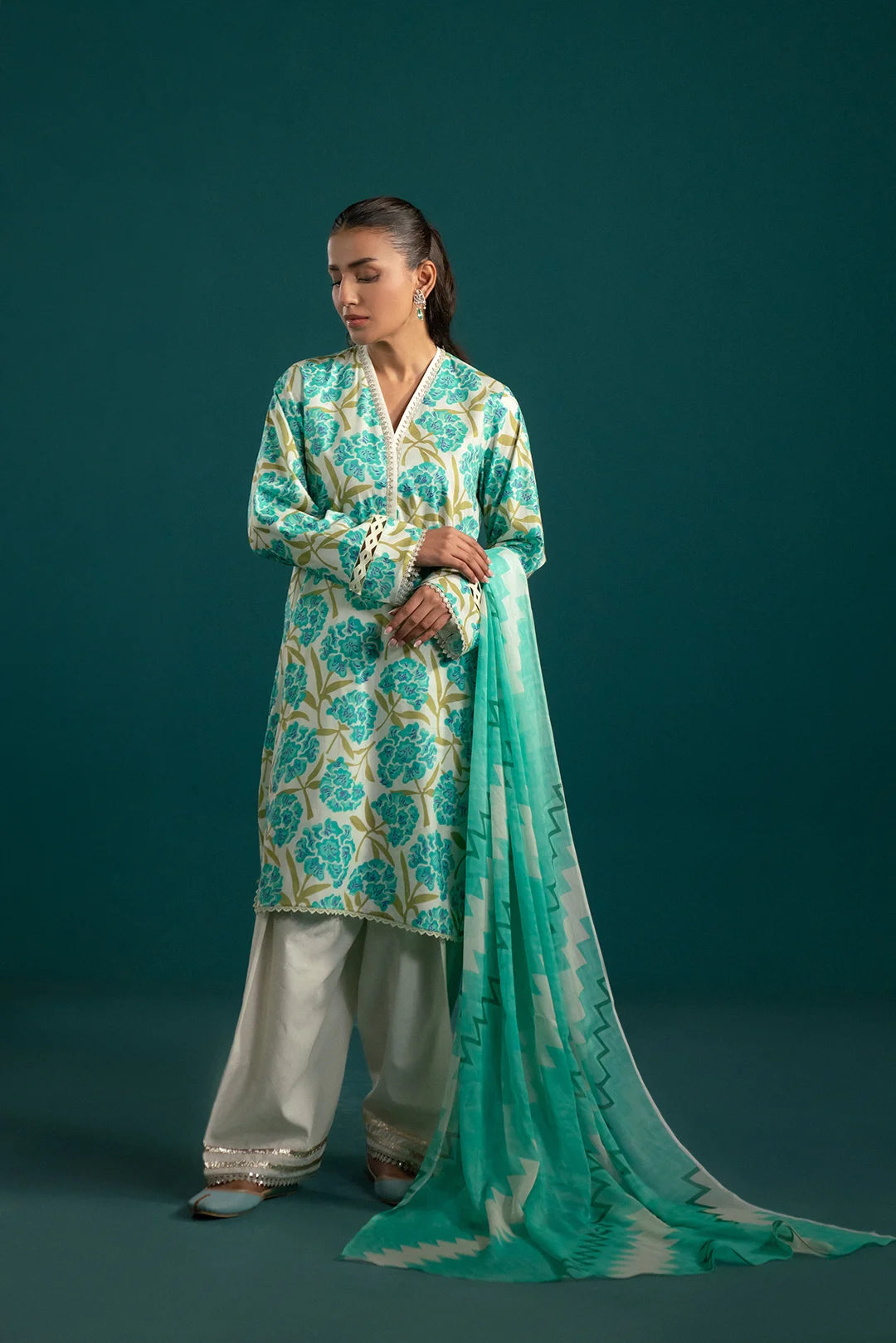 Elegant three piece lawn suit featuring an off-white base with sea blue floral prints, paired with a zigzag chiffon dupatta and dyed cambric trouser – a must-have for summer.