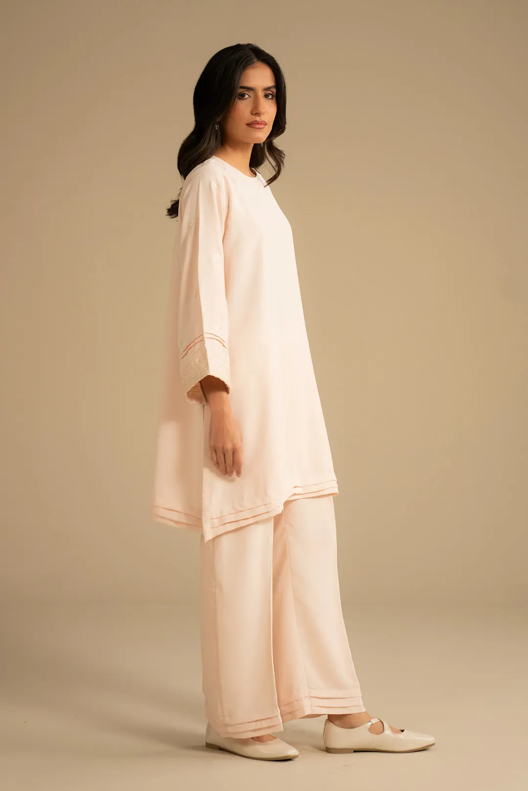 Full-length side/front pose of peach 2 piece suit showing straight trousers and hem finish.