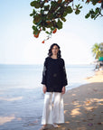 Full-length view of black embroidered linen shirt with white trousers on the beach