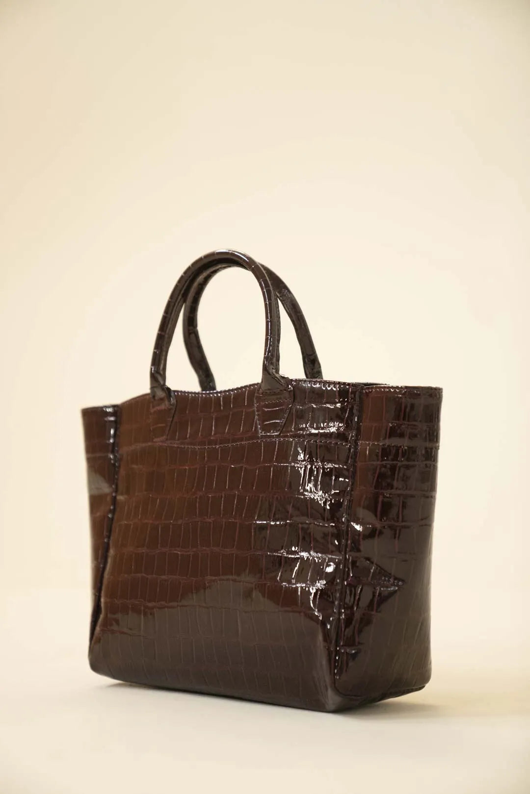 Glossy brown crocodile-embossed tote bag with double top handles, shown in a clean studio setting.
