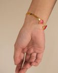 Gold-tone open cuff bracelet with pink enamel floral ends, worn on wrist (front angle).