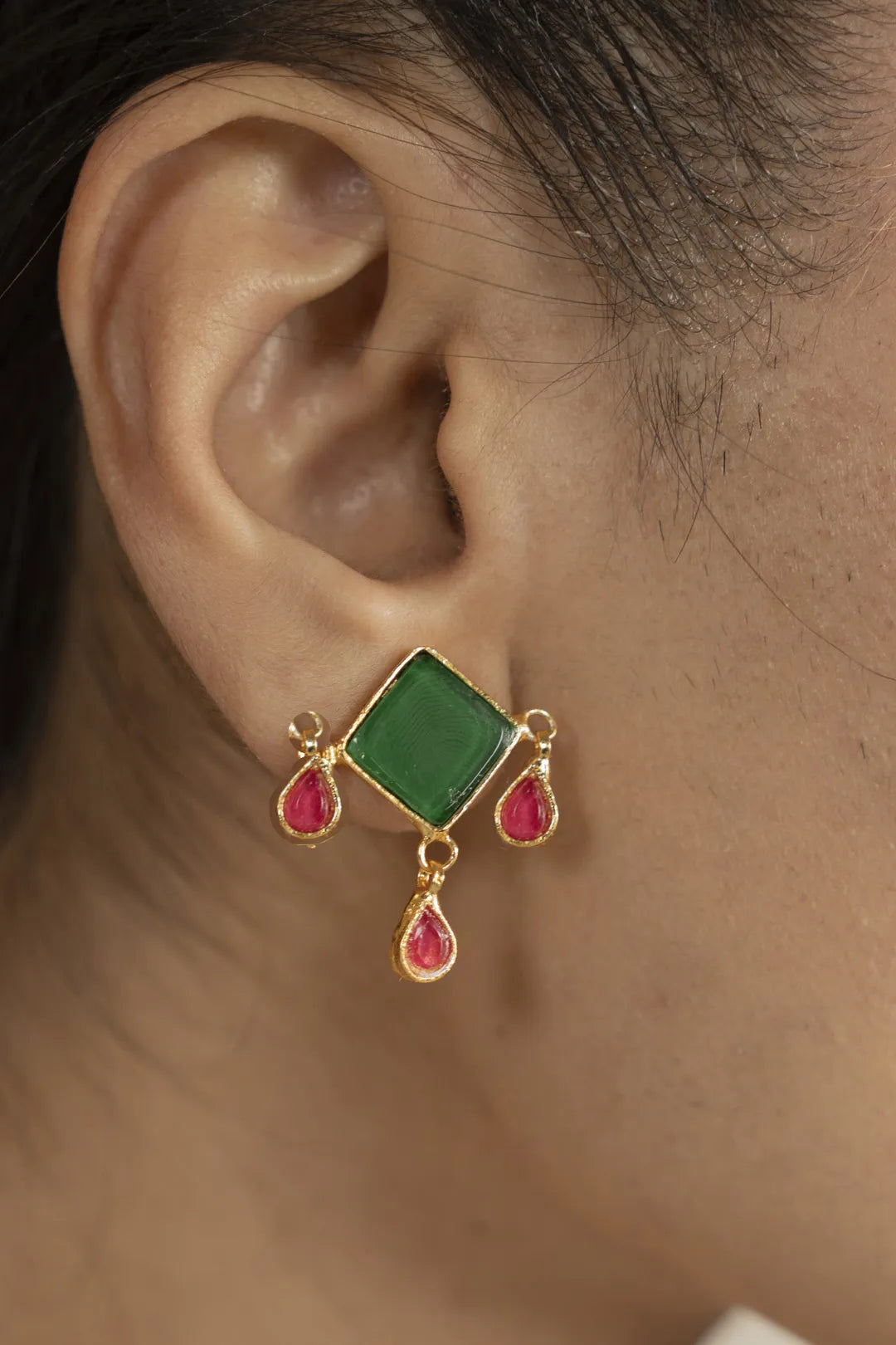 Green kundan stud earring with red teardrop dangles, worn on ear close-up.