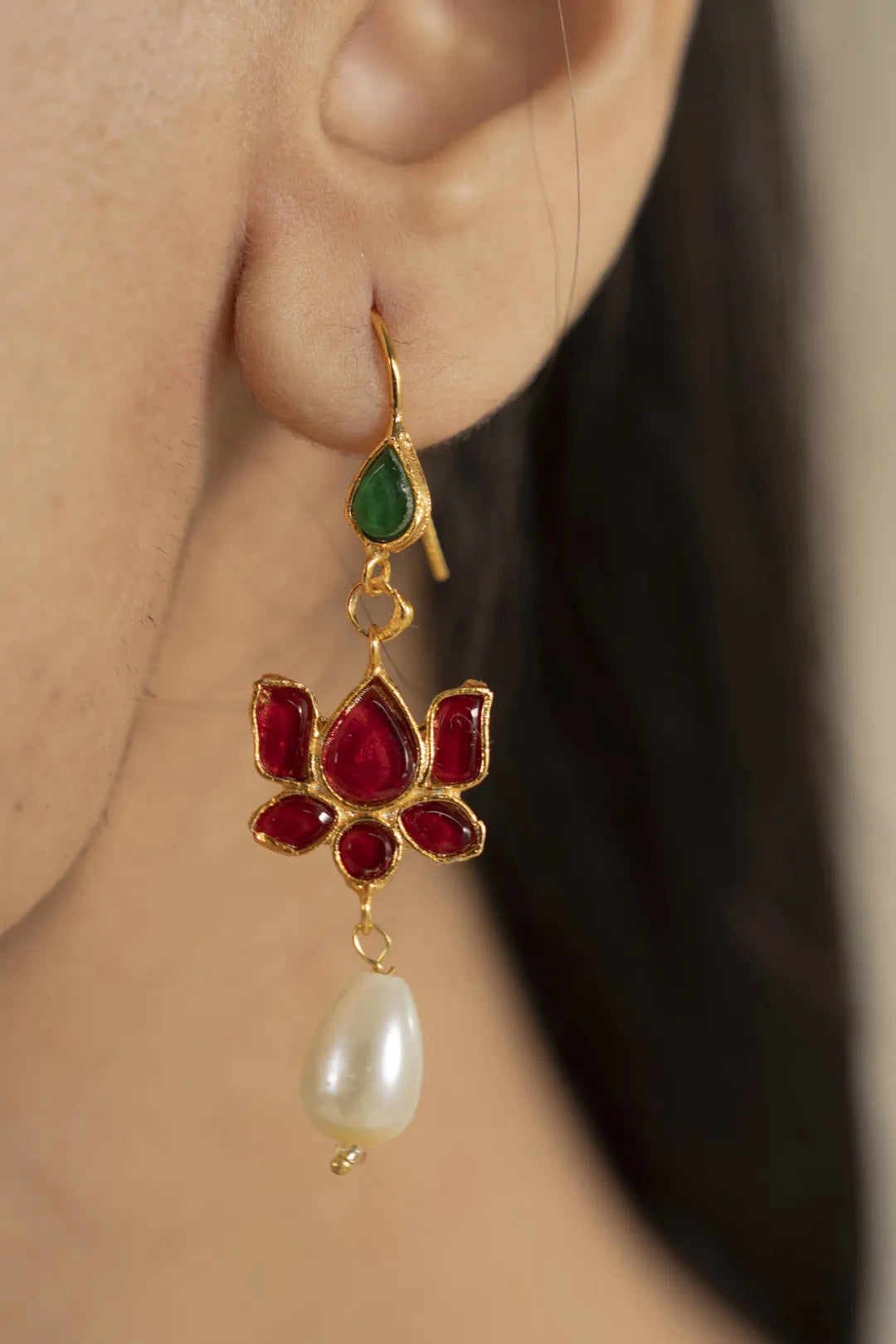 Lotus kundan drop earring with red floral stones, green top accent and pearl dangle, worn on ear close-up.