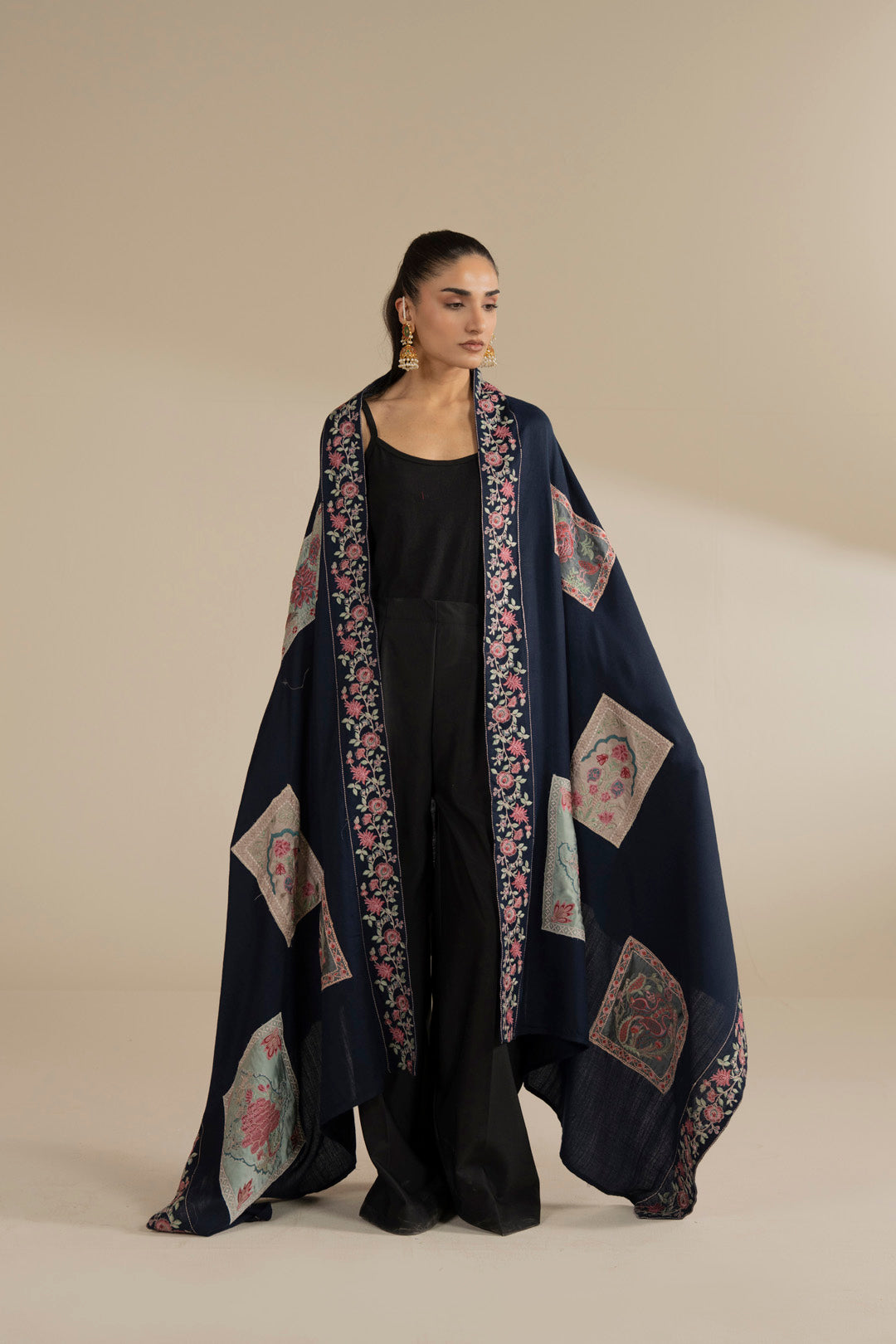 Model wearing blue yarn dyed shawl with embroidered border and large motif panels, draped over a black outfit in studio