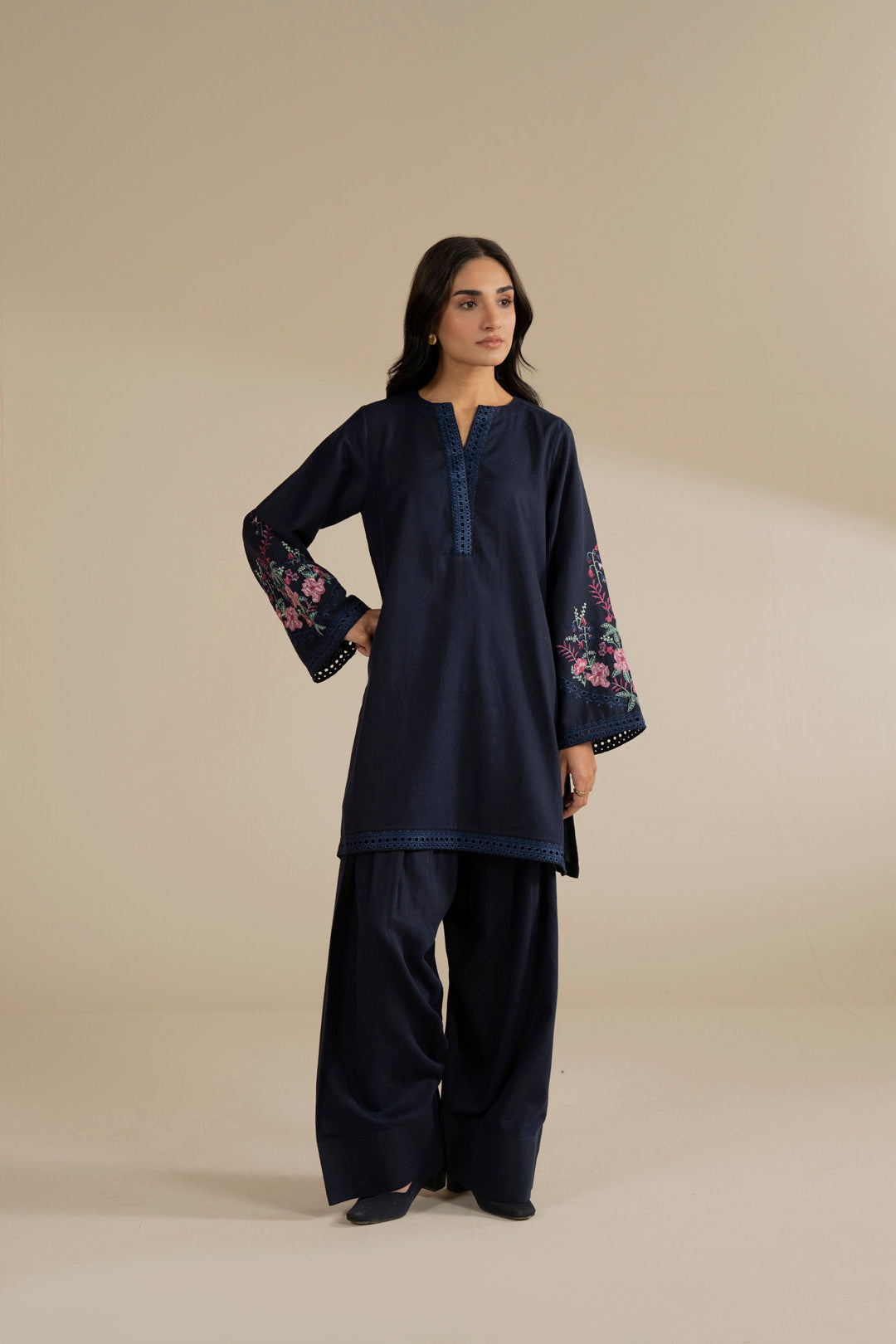 Model wearing navy blue 2 piece embroidered suit with floral sleeves, full front view in studio.