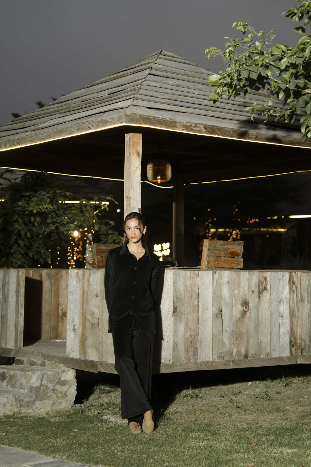 Outdoor full-length view of black velvet co-ord set near wooden structure, showing overall silhouette.