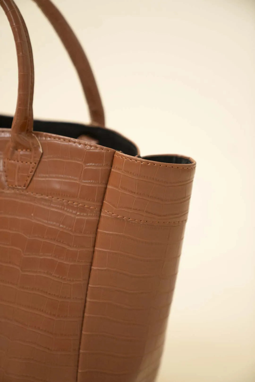 Side detail of brown croc-textured tote bag showing structured shape and sturdy handles in studio lighting