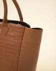 Side detail of brown croc-textured tote bag showing structured shape and sturdy handles in studio lighting