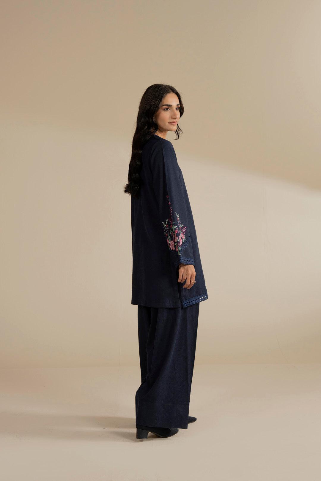 Side pose of model in navy blue 2 piece embroidered suit, showing drape and fit.