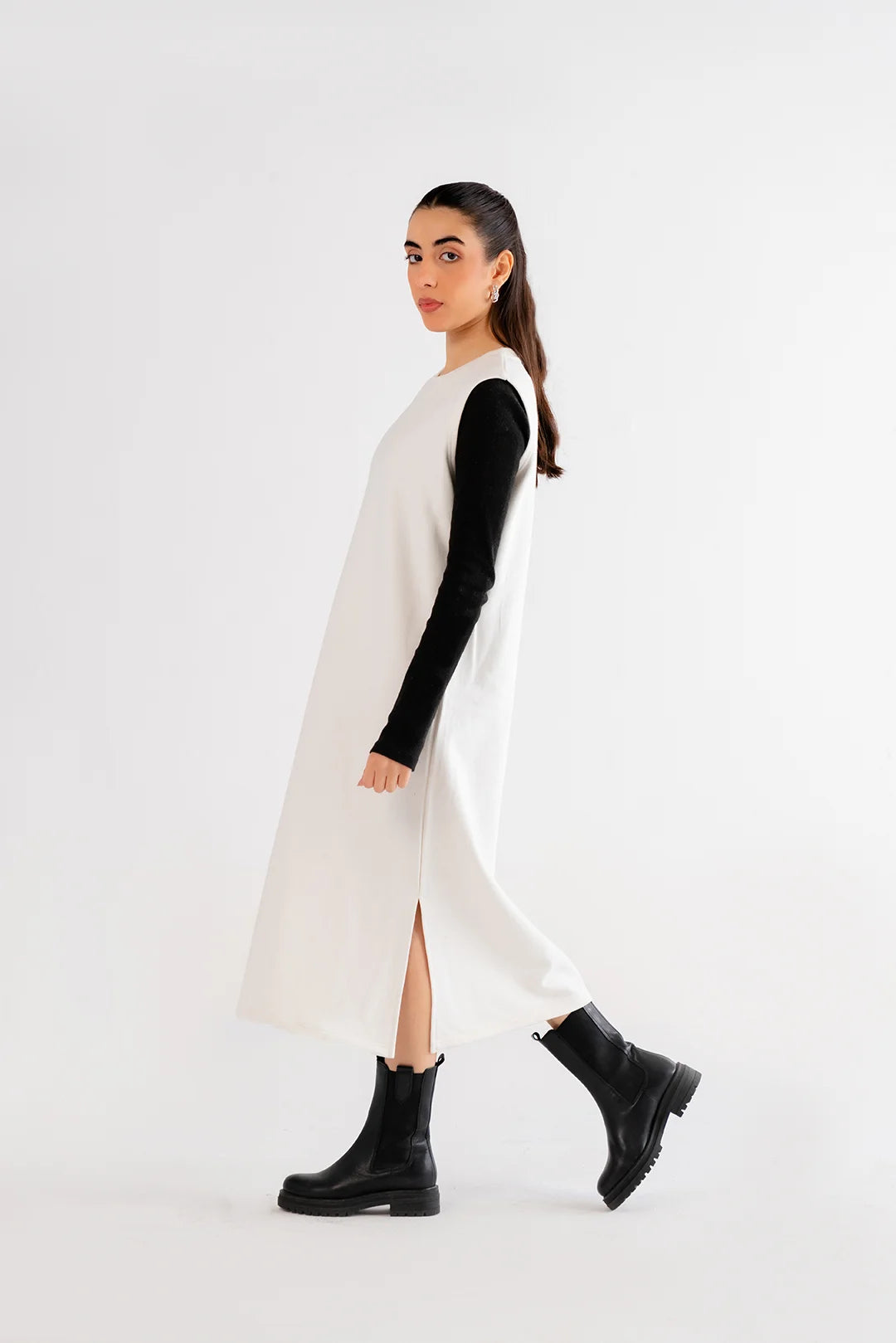 Woman wearing a white maxi dress with black long sleeves, styled with black ankle boots for a modern look