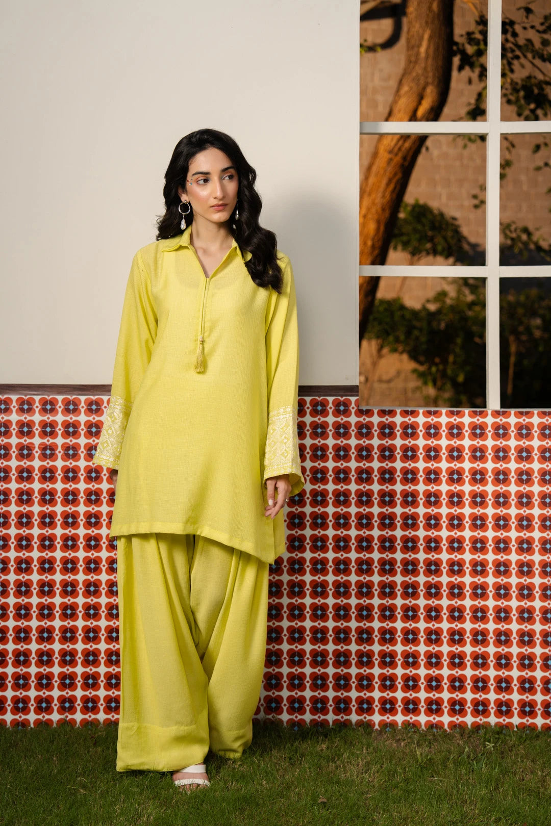 Woman wearing a bright yellow embroidered ready-to-wear kurta with matching trousers, standing in front of a decorative tiled backdrop — Beyond East Fall Winter pret collection