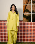 Woman wearing a bright yellow embroidered ready-to-wear kurta with matching trousers, standing in front of a decorative tiled backdrop — Beyond East Fall Winter pret collection