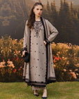 Woman wearing a grey linen suit with black floral embroidery on the front panel and sleeves, paired with a grey and black dupatta, standing in an autumn garden with mountain backdrop — Beyond East Winter Tale collection