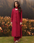 Woman wearing a deep red embroidered linen suit with flowing silhouette, standing in a field of wildflowers with mountains in the background
